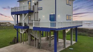 Una casa de dos pisos con un balcón en el nivel superior, construida sobre pilotes cerca de una playa.