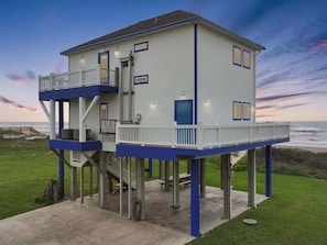 A two-story house with a balcony on the upper level, situated on stilts near a beach. - Beachfront Home w/ 180 Degree Views | Private (Crystal Beach)