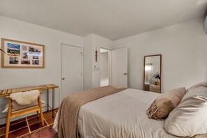 Ein Schlafzimmer mit einem Bett, einem Schreibtisch, einem Stuhl, einem Spiegel und einem Wandbild.