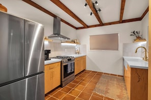 A kitchen with stainless steel appliances, wooden cabinets, a tiled floor, and a window with blinds. - Boulder Oasis - 3 Bed 2 Bath Home in Yucca Valley (Yucca Valley)