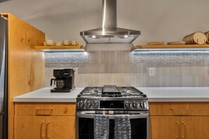 A modern kitchen with a stainless steel range hood, a coffee maker, and wooden cabinets. - Boulder Oasis - 3 Bed 2 Bath Home in Yucca Valley (Yucca Valley)