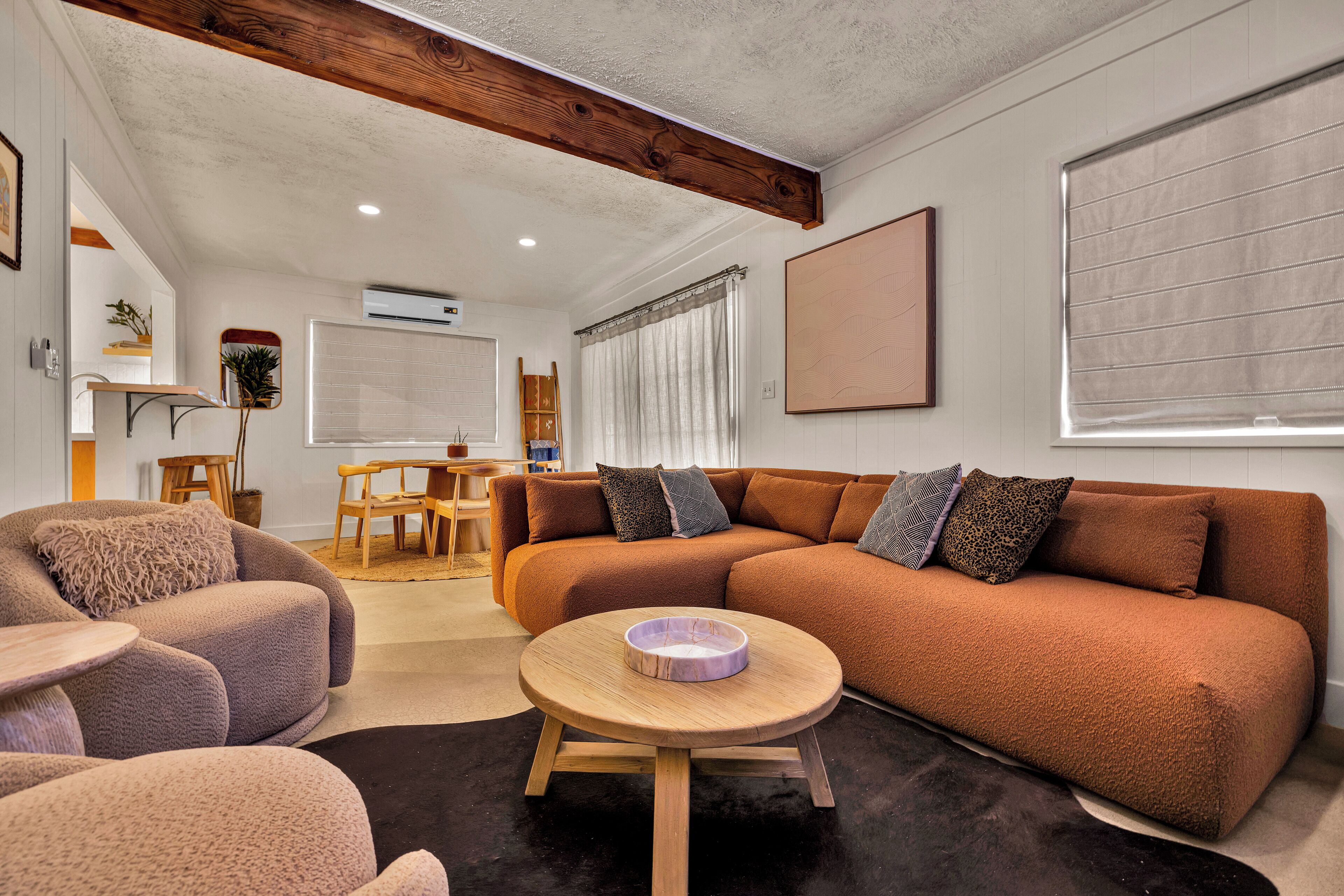 A modern living room with a brown sofa, a round wooden coffee table, and a black rug.