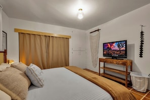 A bedroom with a bed, a television on a wooden stand, a wardrobe, and a wall-mounted decor piece. - Boulder Oasis - 3 Bed 2 Bath Home in Yucca Valley (Yucca Valley)