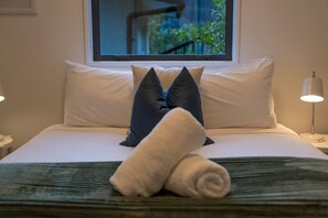 A neatly made bed with white linens, a rolled towel, and two pillows, one dark and one light, with a window in the background. - Queenstown Quarters - Residence I (Queenstown)
