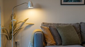 Un salón con un sofá gris, varios cojines, una lámpara de pie y una planta.