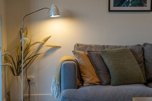 Ein Wohnzimmer mit grauem Sofa, mehreren Kissen, einer Stehlampe und einer Pflanze.