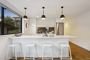 A modern kitchen with a central island, bar stools, pendant lights, and a stainless steel refrigerator. - Queenstown Quarters - Residence I (Queenstown)