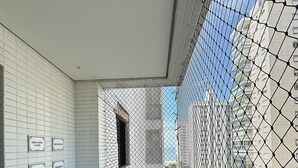 A balcony with two chairs, white tiled walls, and a view of buildings through a mesh screen. - SHB Paraíso em Pitangueiras  (Guarujá)