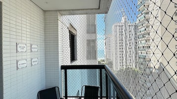 A balcony with two chairs, white tiled walls, and a view of buildings through a mesh screen.