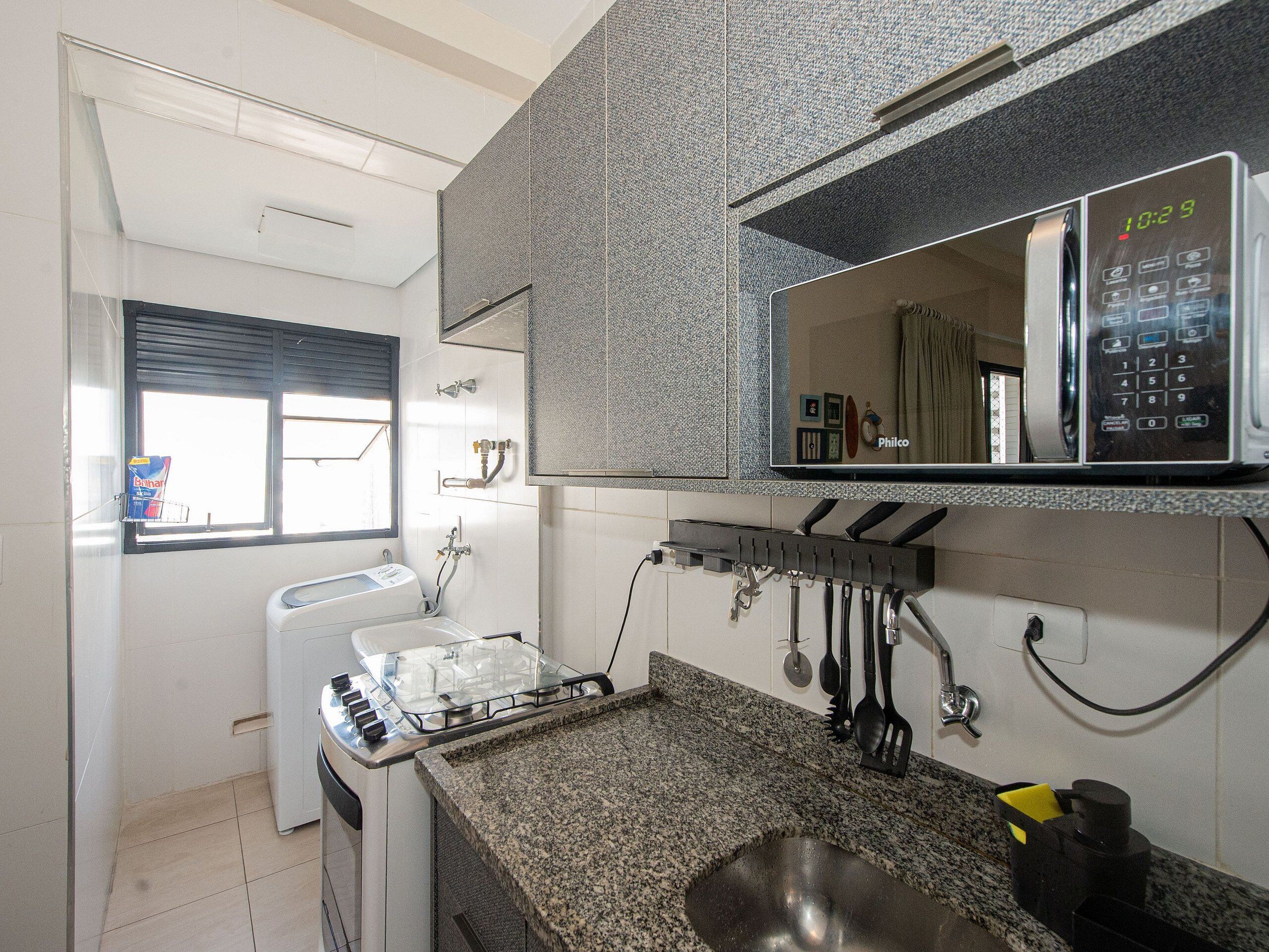 Una cocina con encimera de granito, microondas, estufa a gas y ventana con persianas.
