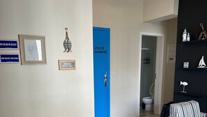 A modern living room with a white table set for two, a blue sofa, and a door labeled 'VOLTE SEMPRE'. - SHB Paraíso em Pitangueiras  (Guarujá)