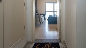 A hallway leading to a living area with a 'hello' mat, a striped chair, and a blue sofa. - SHB Paraíso em Pitangueiras  (Guarujá)