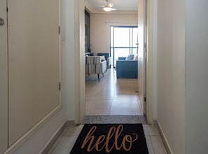 A hallway leading to a living area with a 'hello' mat, a striped chair, and a blue sofa. - SHB Paraíso em Pitangueiras  (Guarujá)