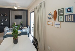 Una sala de estar moderna con un televisor de pantalla plana, una mesa de comedor con una planta en maceta, un sofá y un balcón con cortinas.