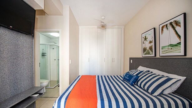 Un dormitorio con cama, televisor, ventilador de techo y ducha.