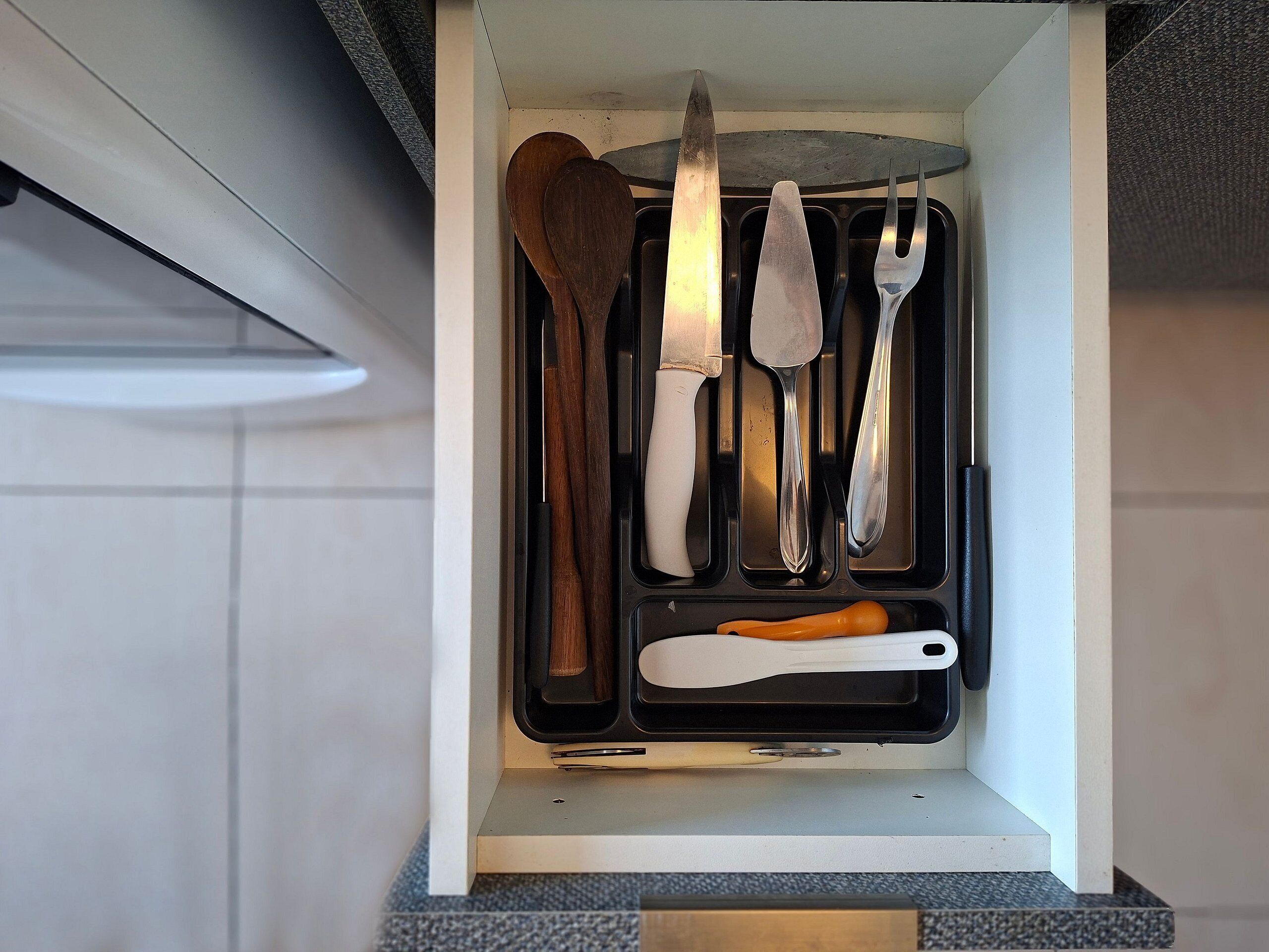 A kitchen drawer with utensils including a knife, spatula, and spoon.