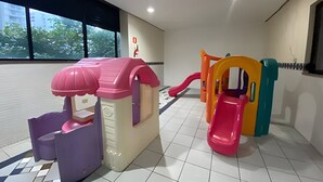 A children's play area with a pink and purple playhouse, a pink slide, and a yellow and green play structure. - SHB Paraíso em Pitangueiras  (Guarujá)