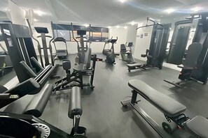 Un gimnasio con diversos equipos de ejercicio, incluyendo cintas de correr, máquinas de pesas y una banca.
