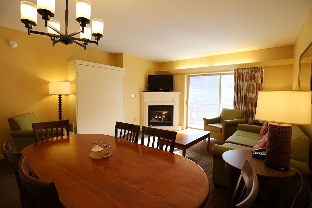 Una habitación de hotel con una mesa de comedor, sillas, una chimenea, un televisor y un sofá.