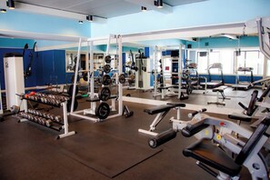 Ein Fitnessstudio mit unterschiedlicher Trainingsausstattung, darunter Kraftgeräte, Kurzhanteln und ein Laufband.