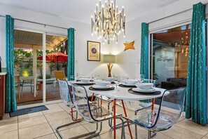 Zona pranzo con tavolo in vetro, sedie, un lampadario e un certificato incorniciato al muro.