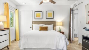A bedroom with a bed, two bedside lamps, a ceiling fan, and two framed pictures on the wall. - 1962 TramView Palm Springs - Poolside Fun, Spa, Fire Pit & Views (Palm Springs)