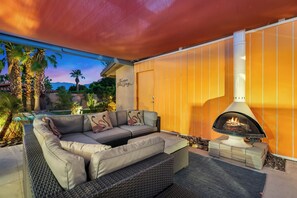 An outdoor seating area with a sofa, a fire feature, and a view of a pool and mountains. - 1962 TramView Palm Springs - Poolside Fun, Spa, Fire Pit & Views (Palm Springs)
