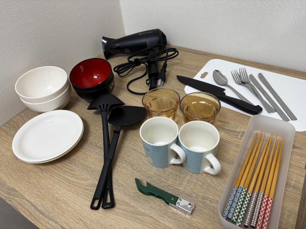 A table with various items including bowls, mugs, chopsticks, a hair dryer, and utensils.