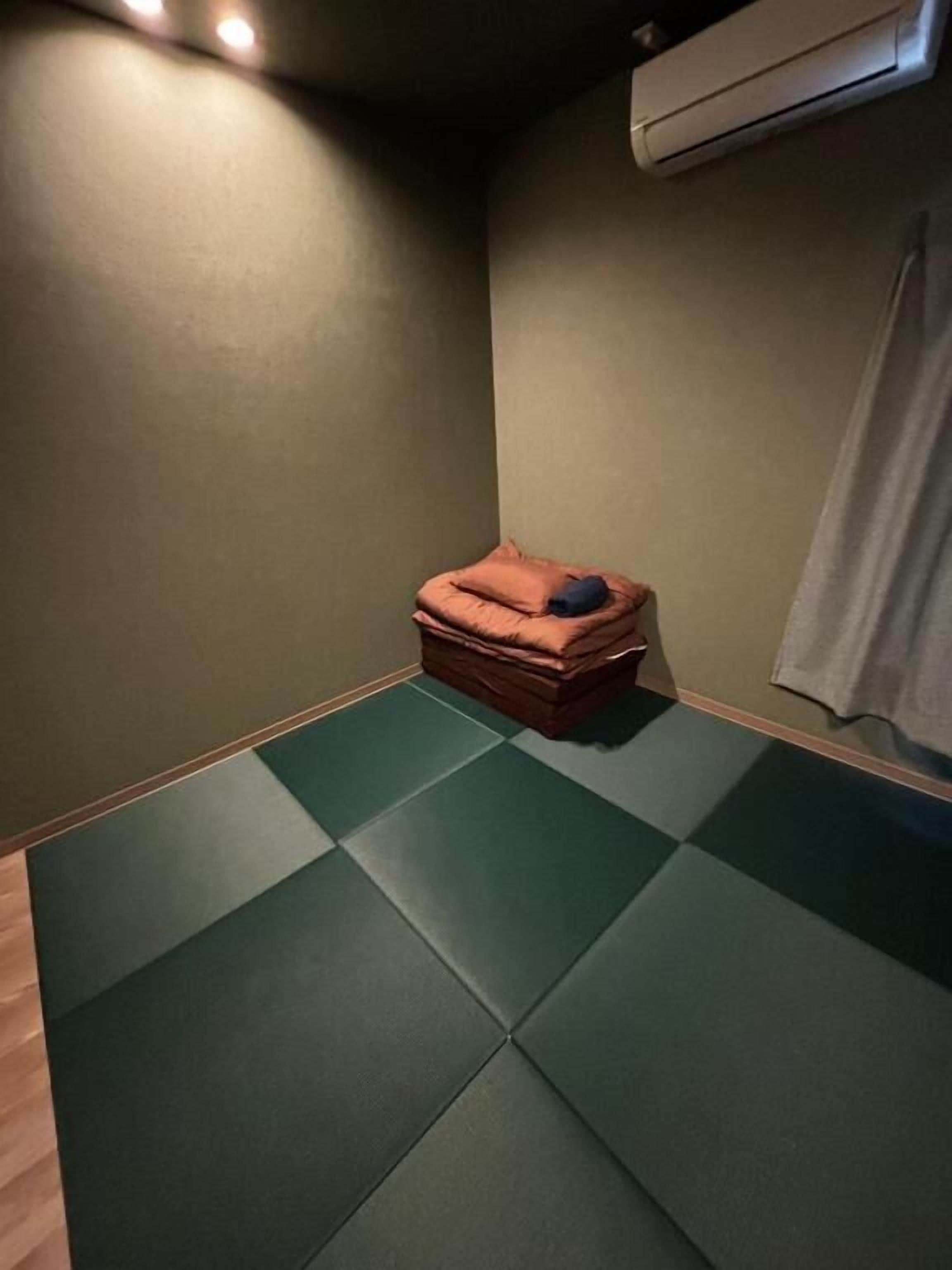 Une pièce dotée d’un sol recouvert de tatamis, d’un petit banc en bois avec des coussins et d’un climatiseur fixé au mur.