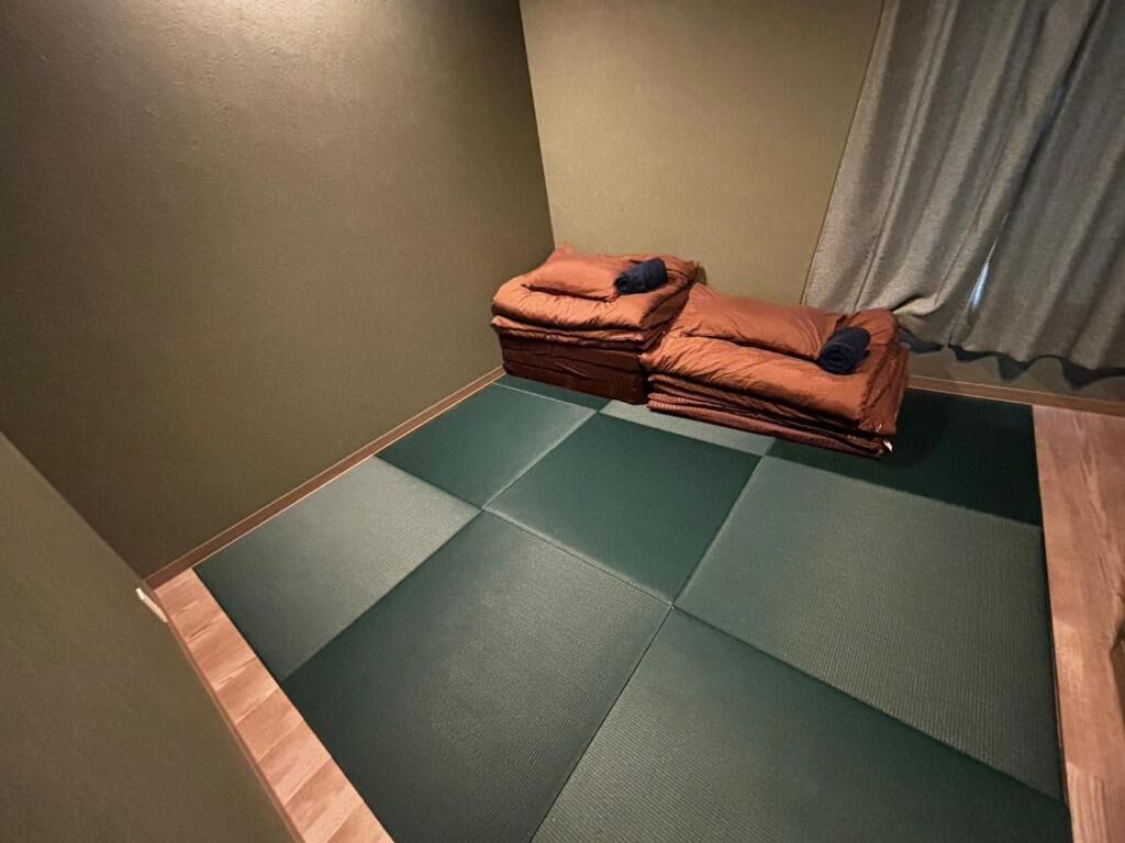 Quarto com esteiras de tatame, um conjunto de esteiras dobradas e uma cortina.