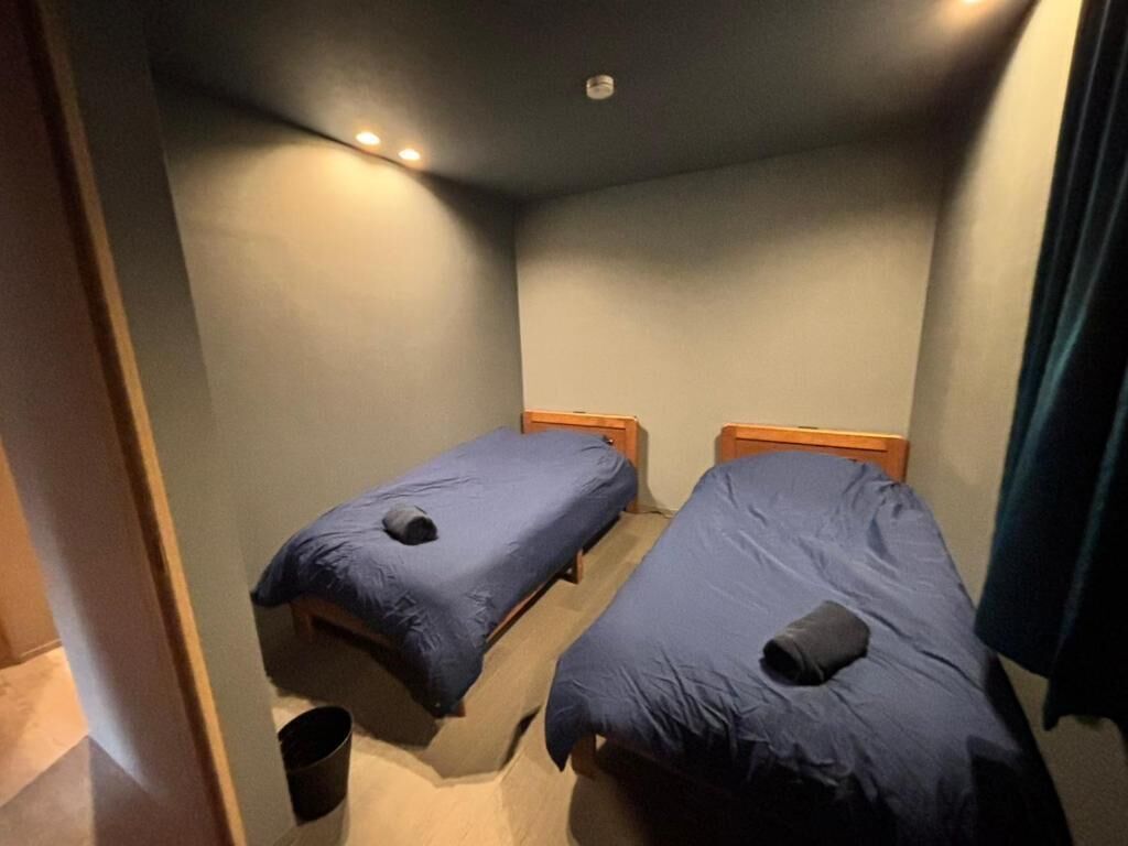 A small room with two single beds, a wooden floor, and a ceiling light.