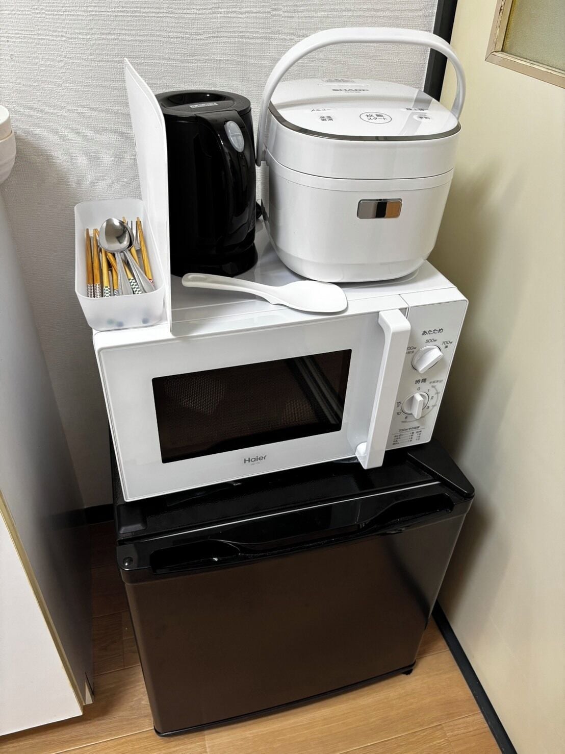 A compact kitchen setup with a microwave, a rice cooker, and a coffee maker.