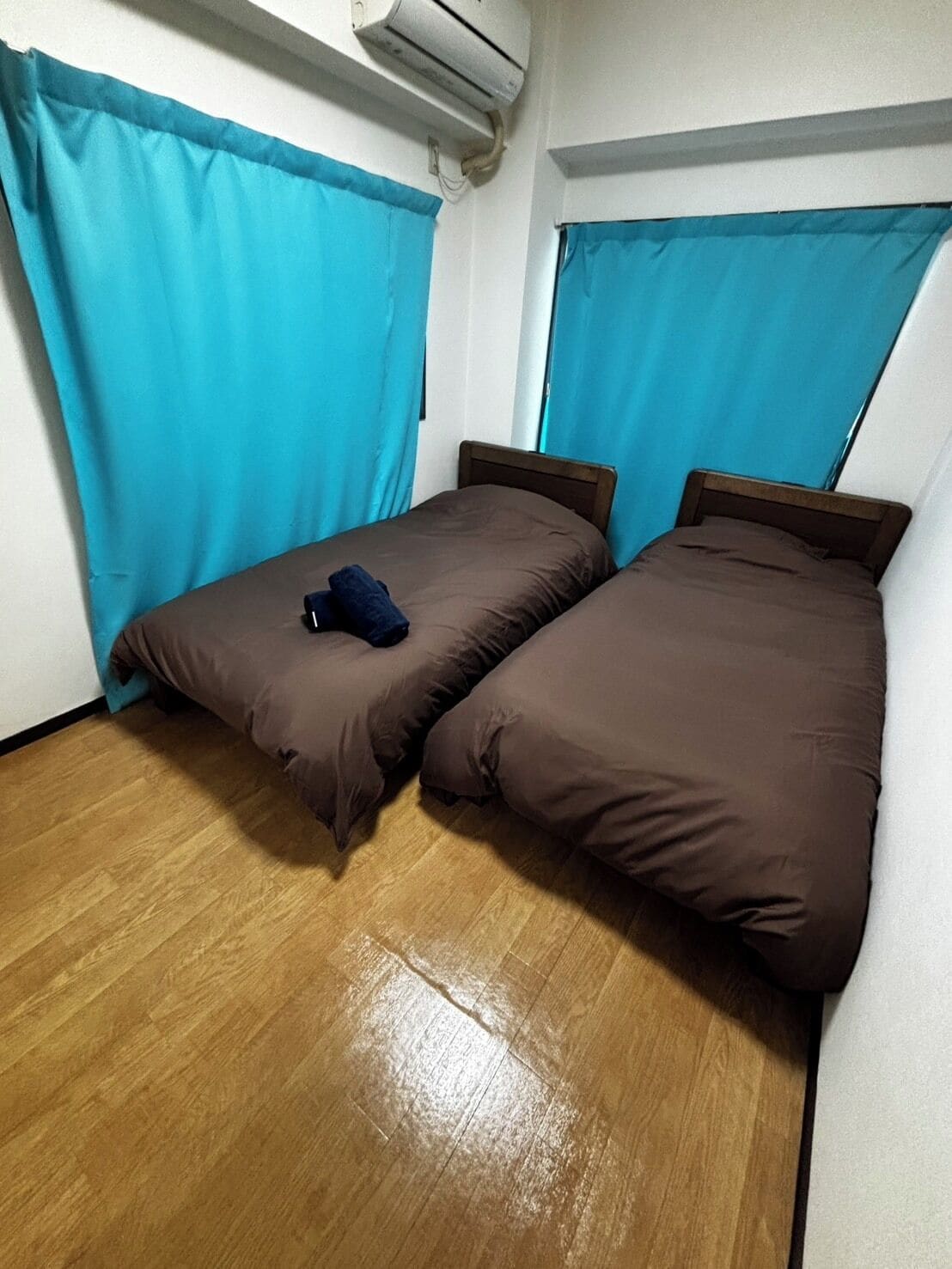 A room with two beds, a wooden floor, and an air conditioning unit on the wall.