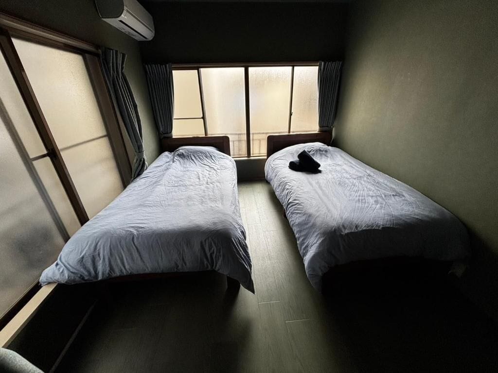 Ein Zimmer mit zwei Einzelbetten, einem fensterbelaubten Fenster und einer Klimaanlage.