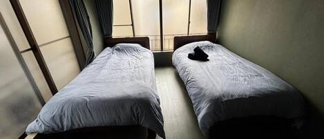 Ein Zimmer mit zwei Einzelbetten, einem fensterbelaubten Fenster und einer Klimaanlage.