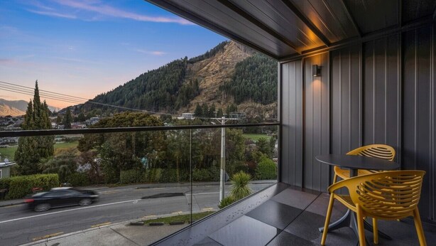 Varanda com vista para uma estrada e montanhas, uma mesa e uma cadeira.