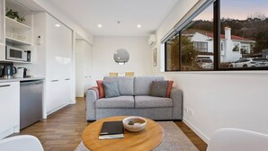Uma sala de estar moderna com um sofá cinzento, uma mesa de centro e vista para uma área residencial por uma janela ampla.