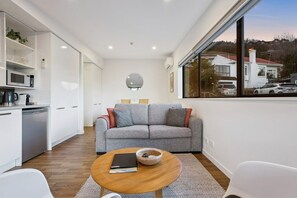 Ein modernes Wohnzimmer mit grauem Sofa, einem Couchtisch und Blick auf eine Wohngegend durch ein großes Fenster.