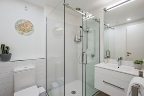 A modern bathroom with a glass-enclosed shower, a white sink, and a large mirror. - Queenstown Quarters - Residence IV (Queenstown)