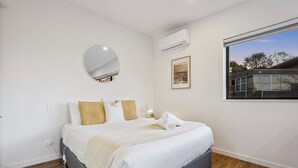 Um quarto moderno com cama, espelho redondo, ar condicionado, quadro emoldurado e janela com vista.
