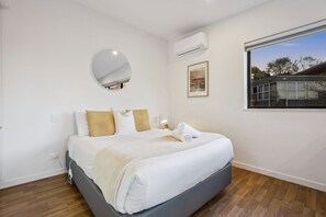 Ein modernes Schlafzimmer mit einem Bett, einem runden Spiegel, einer Klimaanlage, einem gerahmten Bild und einem Fenster mit Blick.
