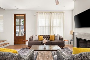 A living room with a sofa, coffee table, patterned armchairs, a fireplace, and a TV. - Germantown Gem | 4BR Home | Sleeps 10 | Minutes to Downtown (Nashville)
