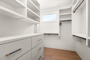 Ein begehbarer Kleiderschrank mit offenen Regalen, einem Fenster und Holzboden.