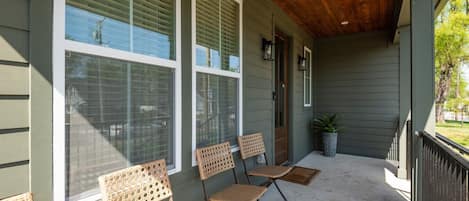 A covered porch with three wicker chairs, a potted plant, and a wooden ceiling.