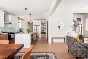 A modern kitchen with white cabinets, a central island, and a dining area with a wooden table and chairs.