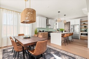 A modern kitchen with white cabinets, a central island, and a dining area with a wooden table and chairs. - Germantown Gem | 4BR Home | Sleeps 10 | Minutes to Downtown (Nashville)