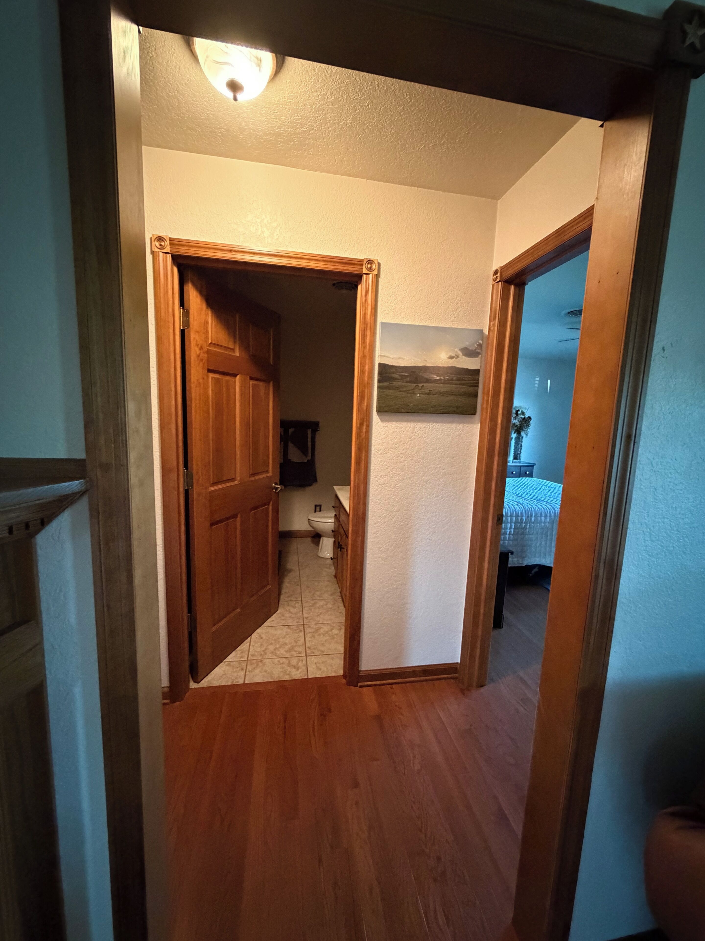 A hallway leading to a bathroom with a toilet, a sink, and a mirror.