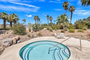 A swimming pool with a stone border, surrounded by desert vegetation and palm trees. - Palm Springs Golf Condo with Pools, Spas, Pickleball, Fire Pit and Mountain Views (Palm Springs)