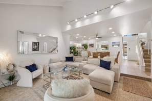 A spacious living room with a large sectional sofa, a glass coffee table, and a white shaggy ottoman. - Palm Springs Golf Condo with Pools, Spas, Pickleball, Fire Pit and Mountain Views (Palm Springs)