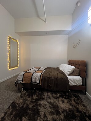 Un dormitorio con una cama, un espejo con iluminación, un tapete mullido y una decoración con la palabra 'love'.